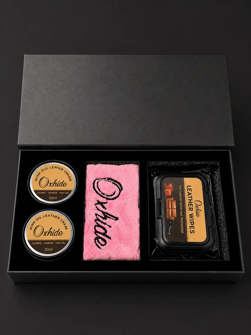 A black leather care gift set in an open black presentation box, featuring two round tins of Orchido leather cream, a pink microfiber cloth with black script, and a black package of leather wipes.